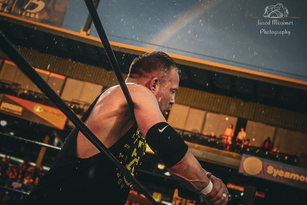 Pro wrestling match action shot showing athletes performing moves in a brightly lit arena.