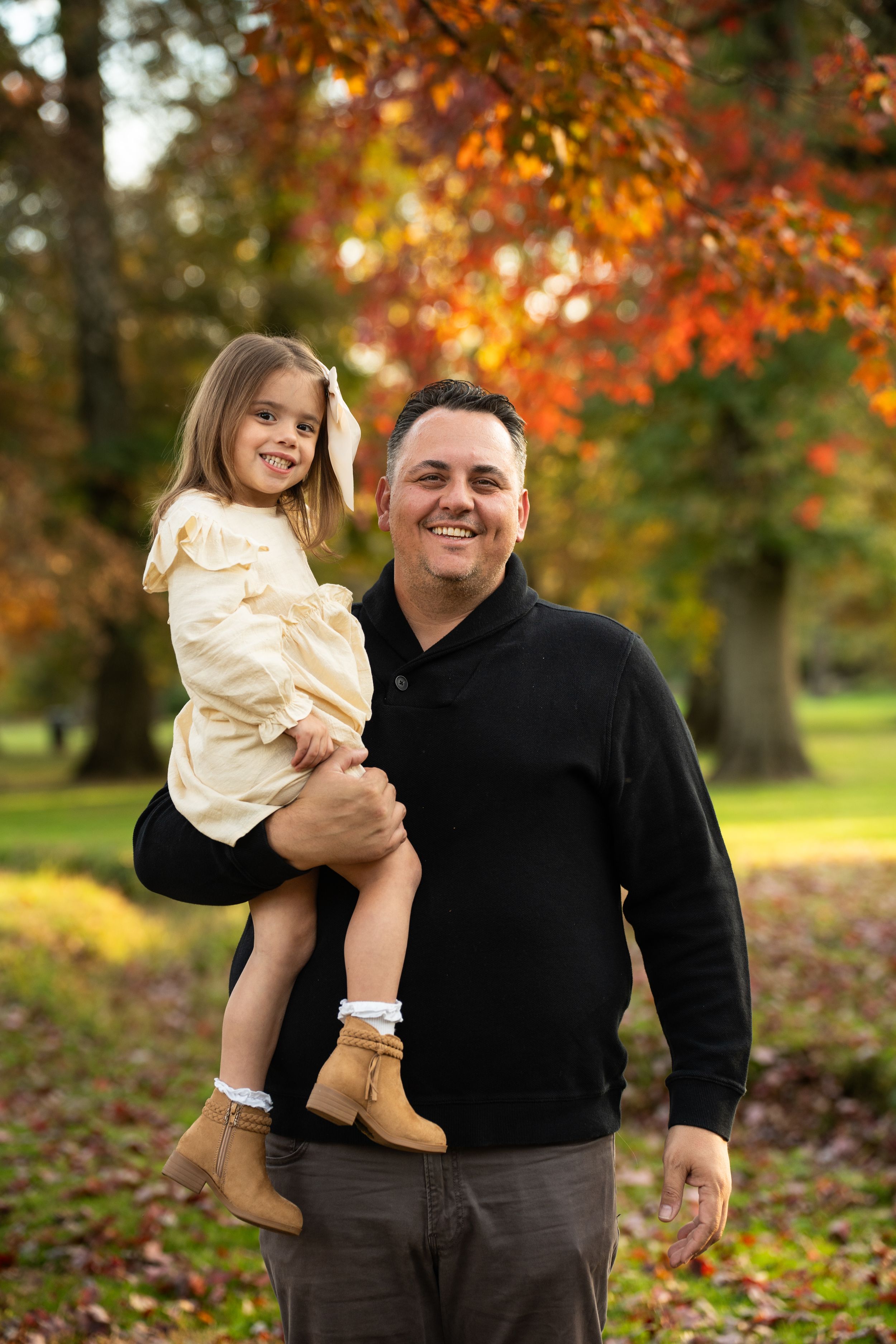 A parent and child playing outdoors in a park during autumn with colorful fall foliage in the background.