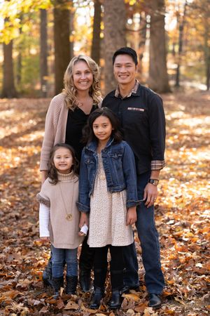 A family poses together on fallen autumn leaves in a scenic forest setting.