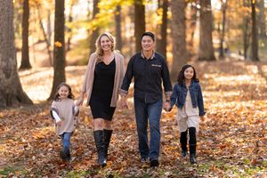 A family walks together holding hands on an autumn path covered in fallen leaves during golden hour at sunset.