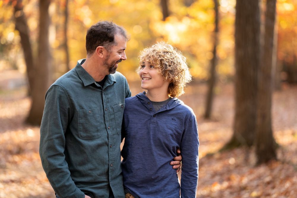 A parent and child share a loving moment while walking through a golden autumn forest.