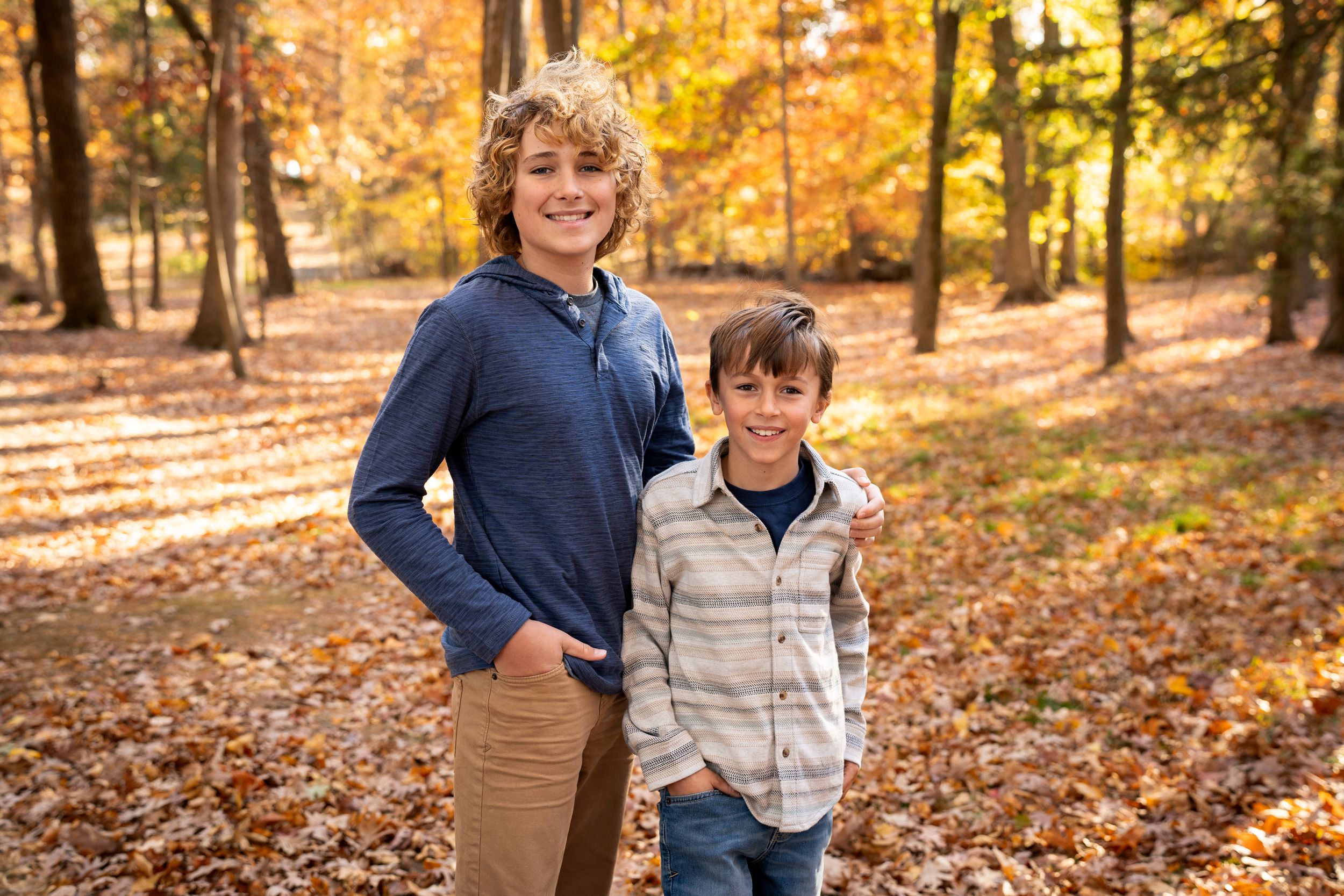 A relaxed group strolls among vibrant fall foliage in a wooded area during golden hour sunlight.
