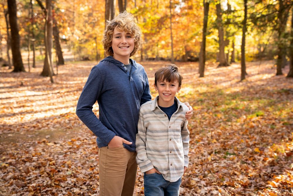 A relaxed group strolls among vibrant fall foliage in a wooded area during golden hour sunlight.