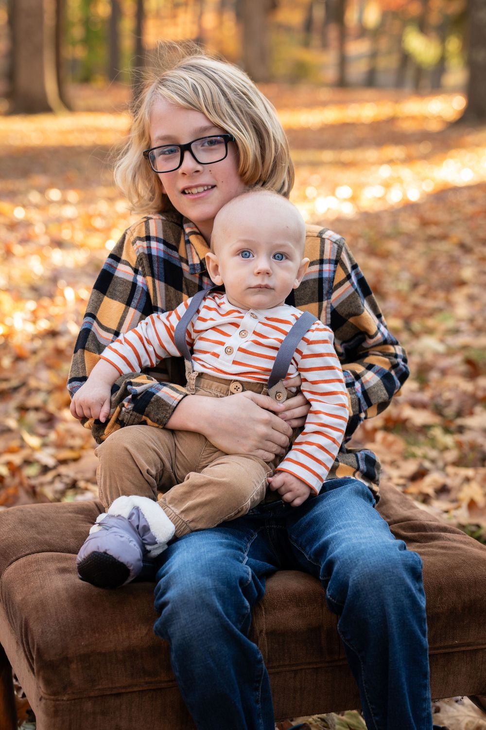 A heartwarming autumn family photoshoot on a brown couch surrounded by fallen leaves in a park setting.