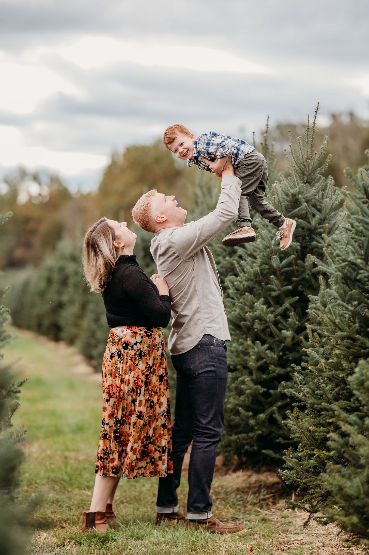 Family shares joyful moment together at Christmas tree farm on cloudy autumn day among evergreen trees.