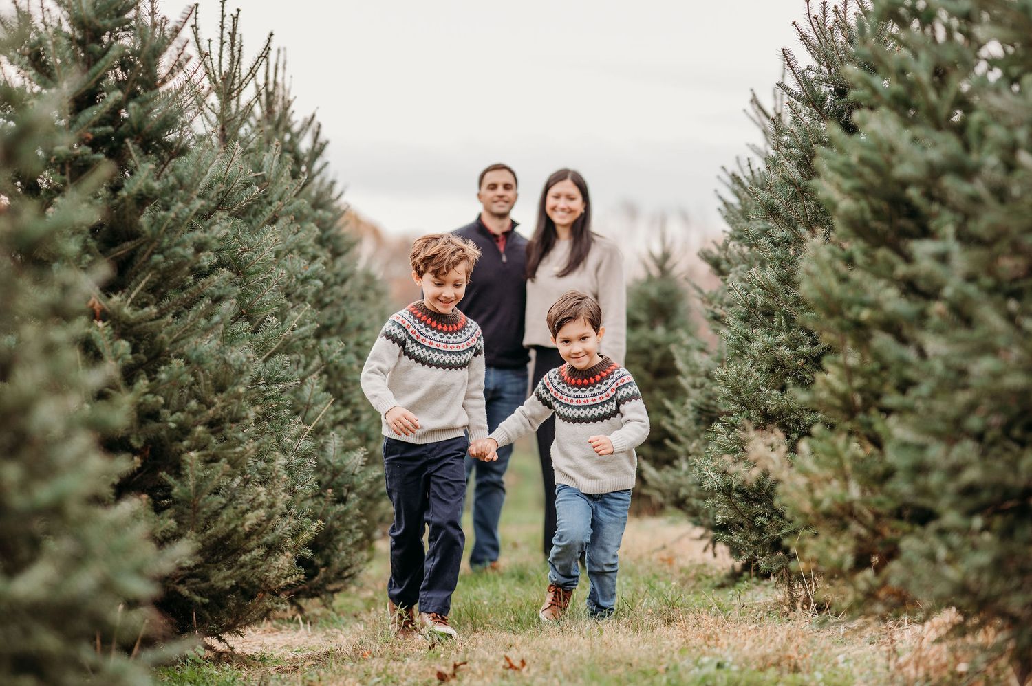 Family enjoying a fun moment together while running between rows of evergreen trees at a Christmas tree farm.