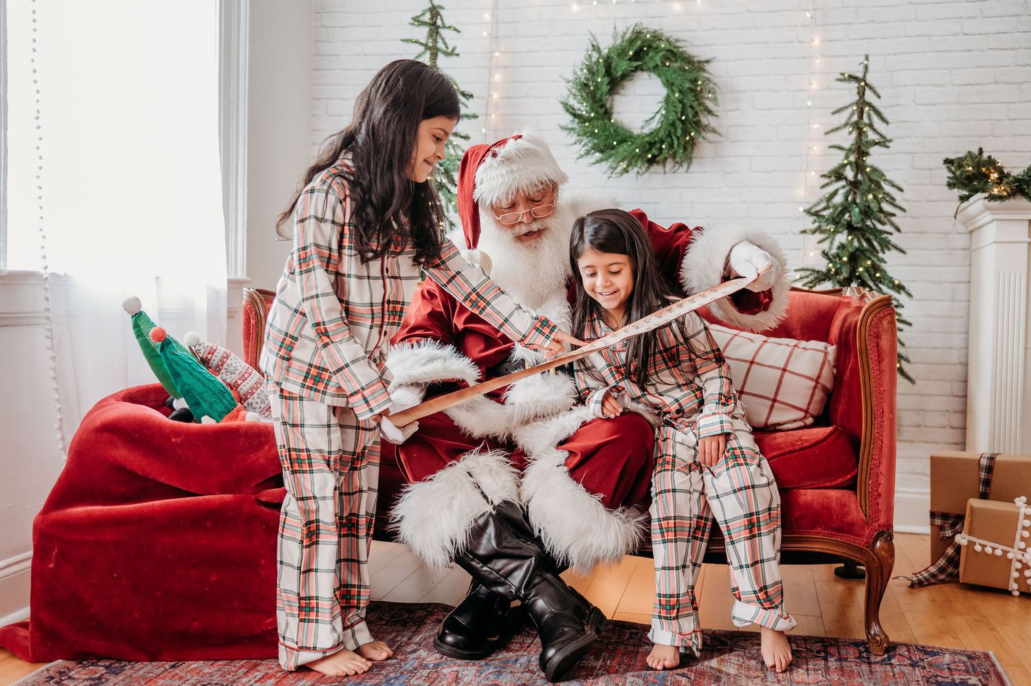 Siters in matching plaid pajamas sit with Santa on red couch during Christmas photos with and find themselves on Santa's nice list.