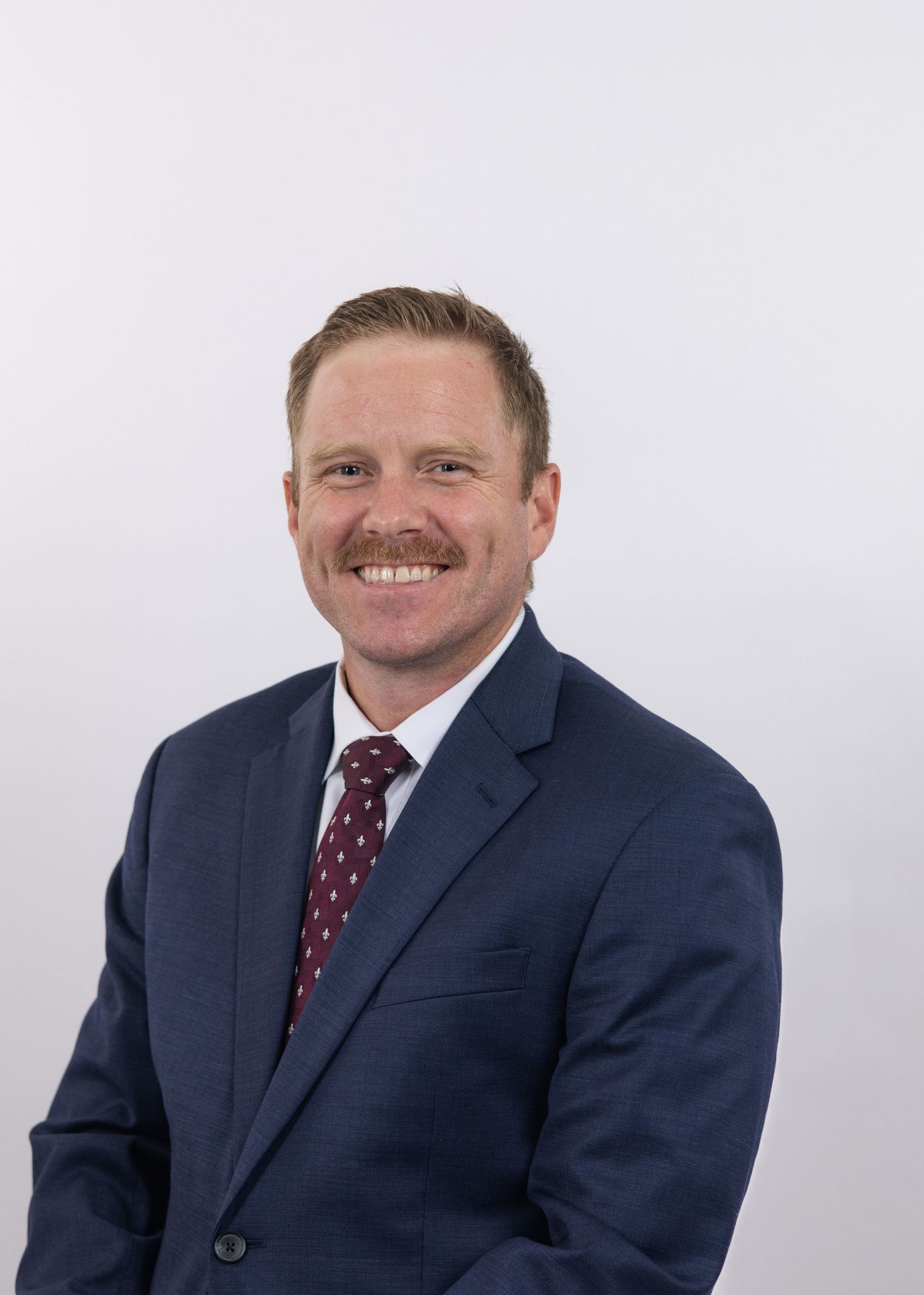 Professional headshots show someone in a navy suit with burgundy tie smiling against a light background.