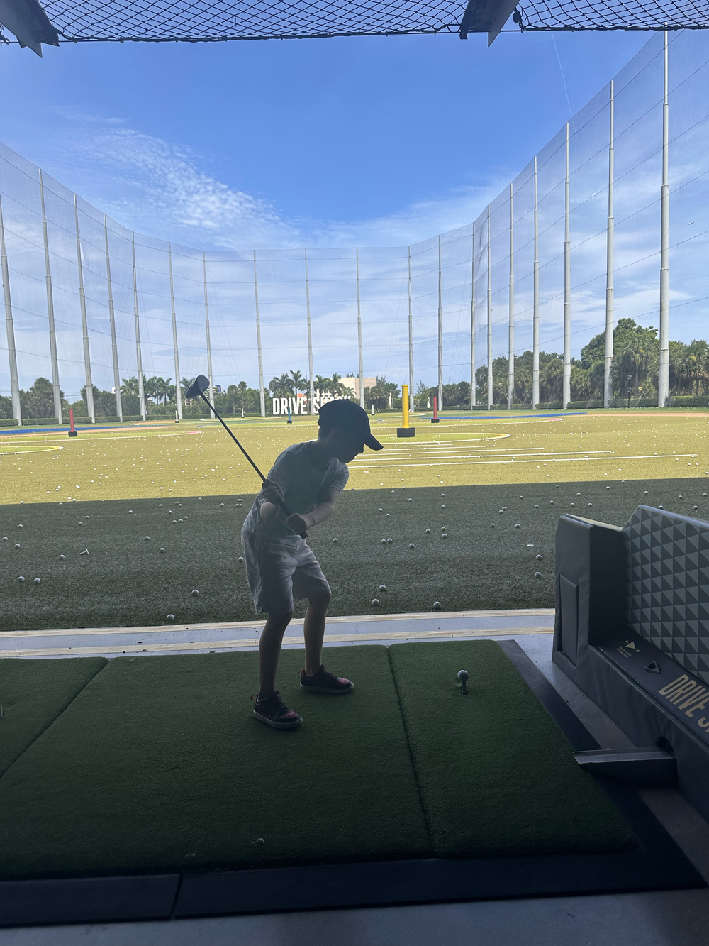 A driving range with high protective netting and hitting bays under blue skies.