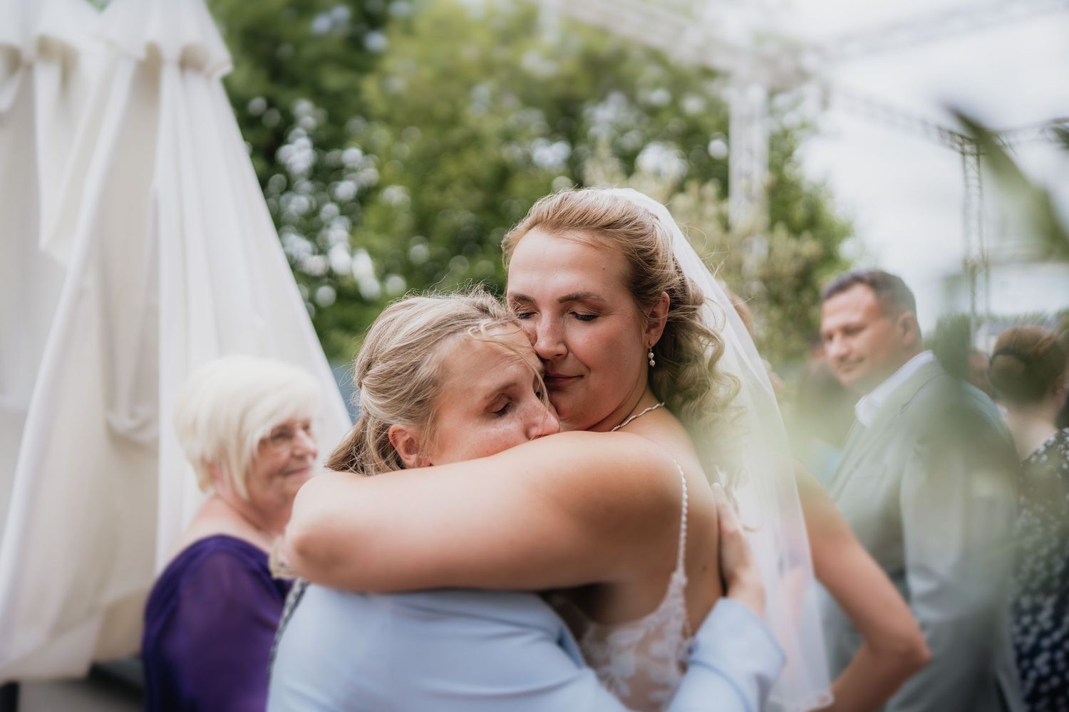 Emotional embrace shared during outdoor wedding reception with white tent visible.