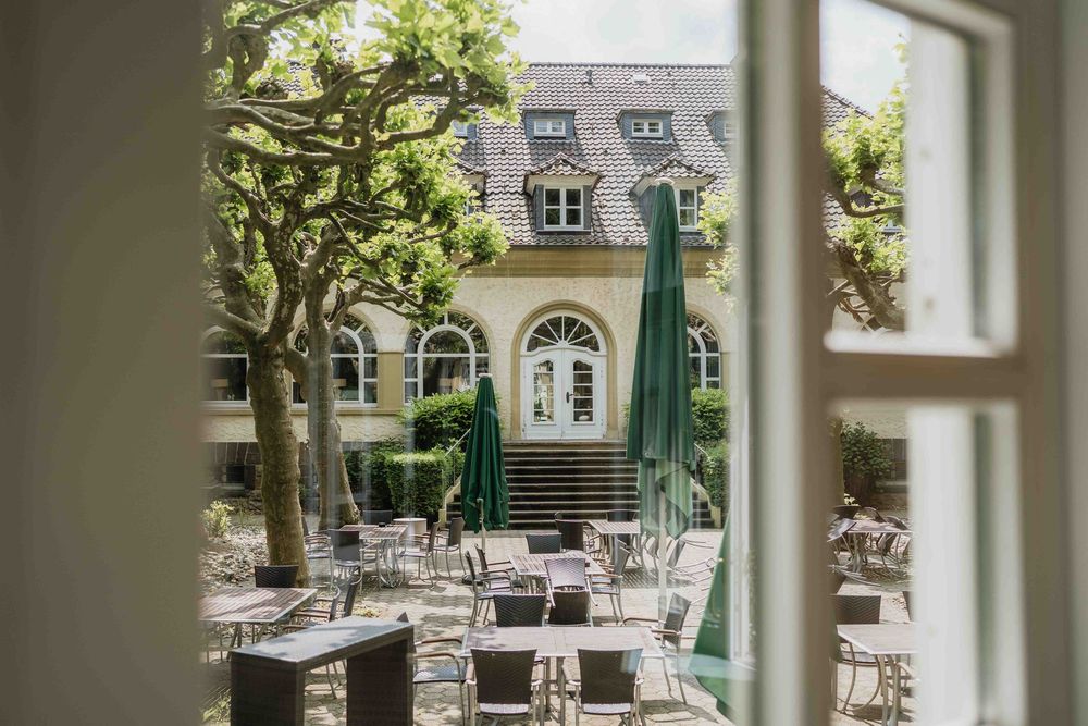 Elegant outdoor wedding reception setup with round tables and chairs on a stone patio surrounded by greenery.