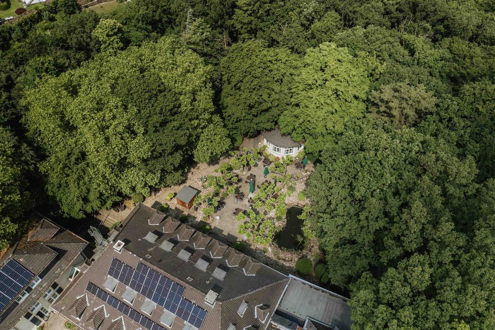 Birds-eye view of solar panels and buildings nestled among dense green trees.