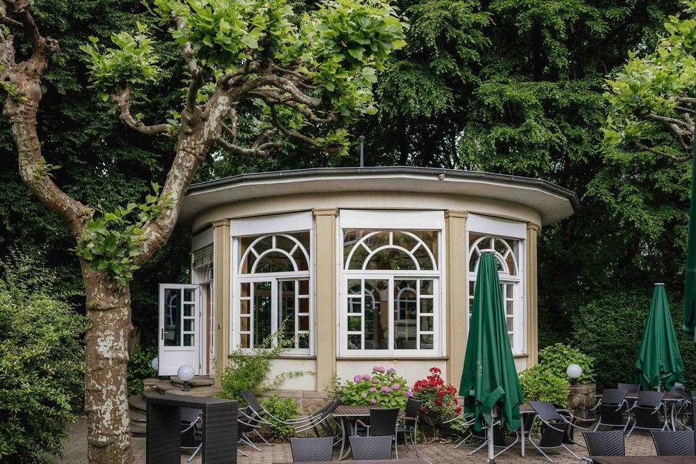 Elegant building exterior with arched windows and outdoor seating area surrounded by trees.