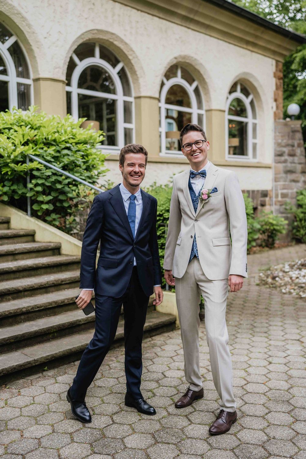 Two people in formal attire standing on stone steps outside a classic building.