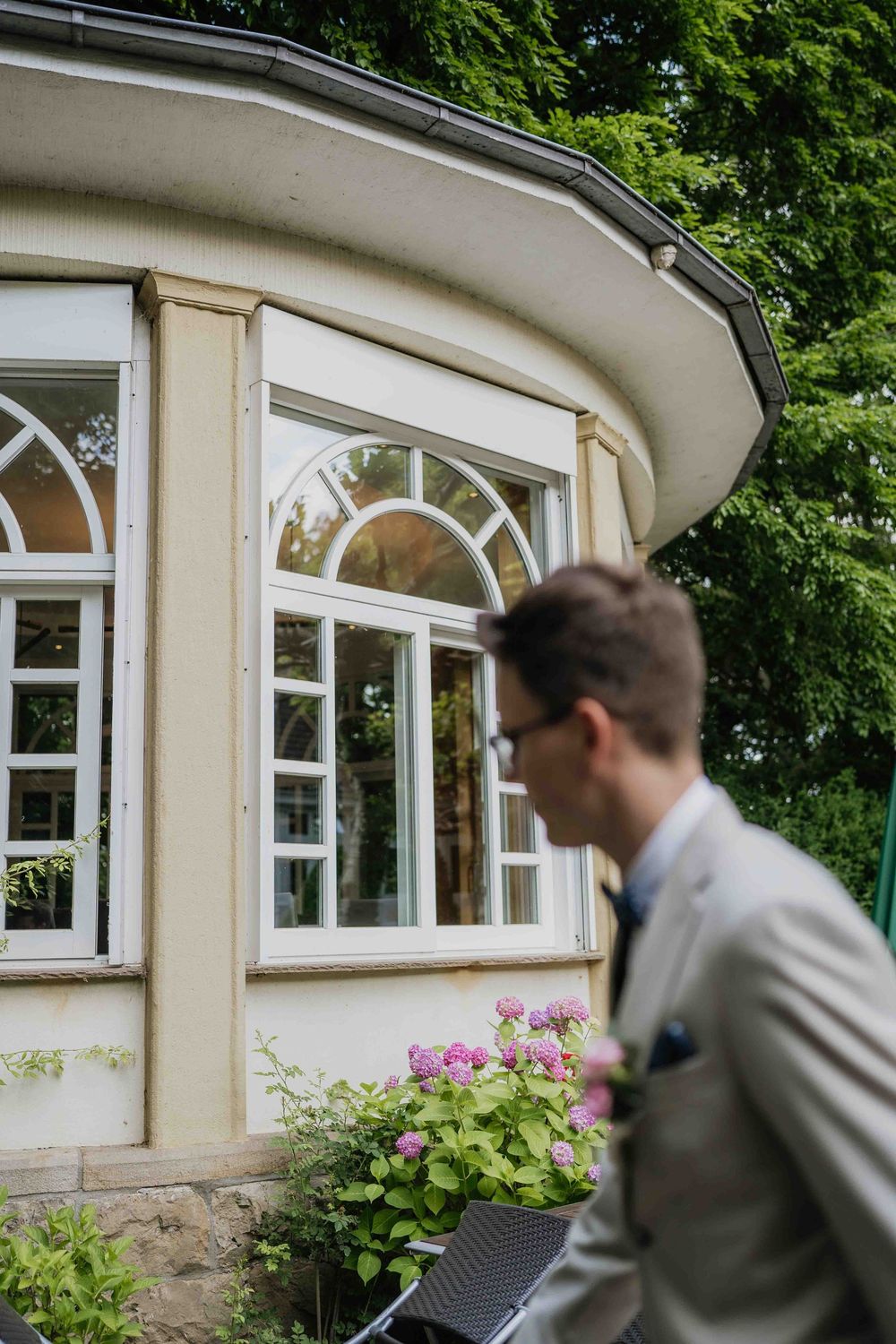 Person in light suit walking past curved architectural windows with blooming flowers.