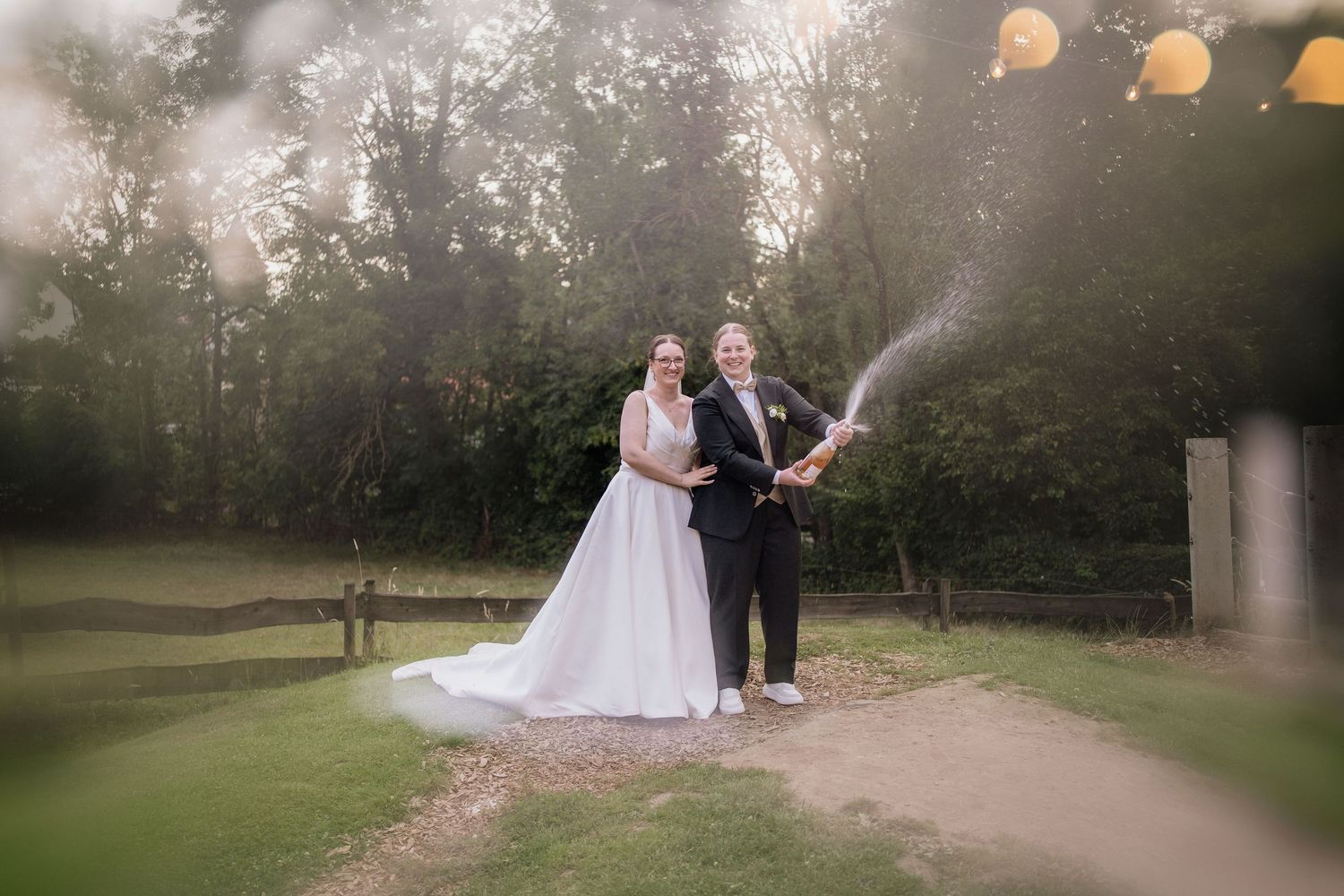 Couple celebrating with champagne spray in an outdoor garden setting.