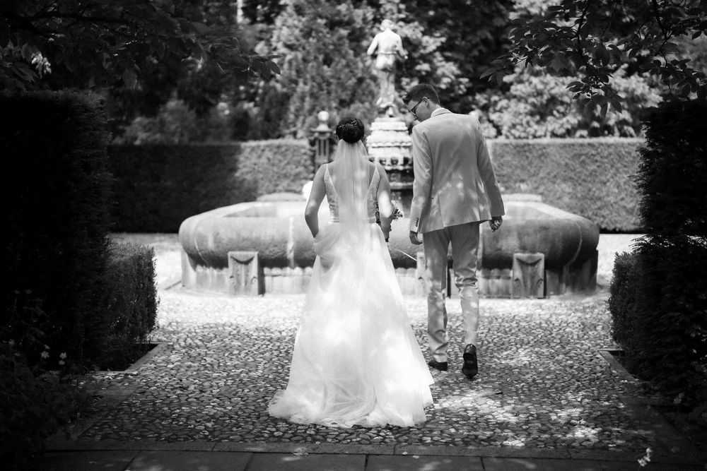 Black and white wide shot of newlyweds walking through garden setting.