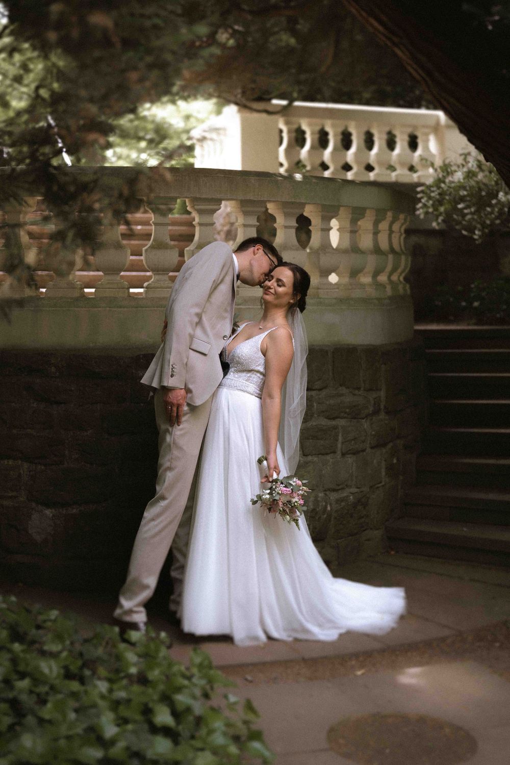 Romantic wedding portrait by stone staircase and ornate balustrade.