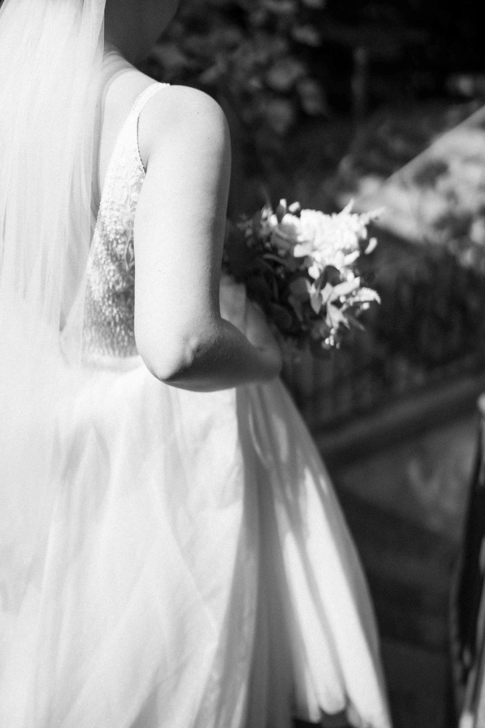 Black and white detail shot of a bride's lace dress and bouquet.