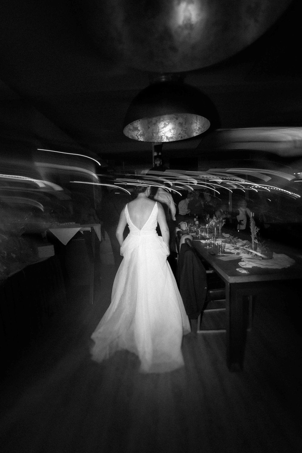 Artistic black and white shot of a bridal gown silhouette in a dimly lit restaurant.