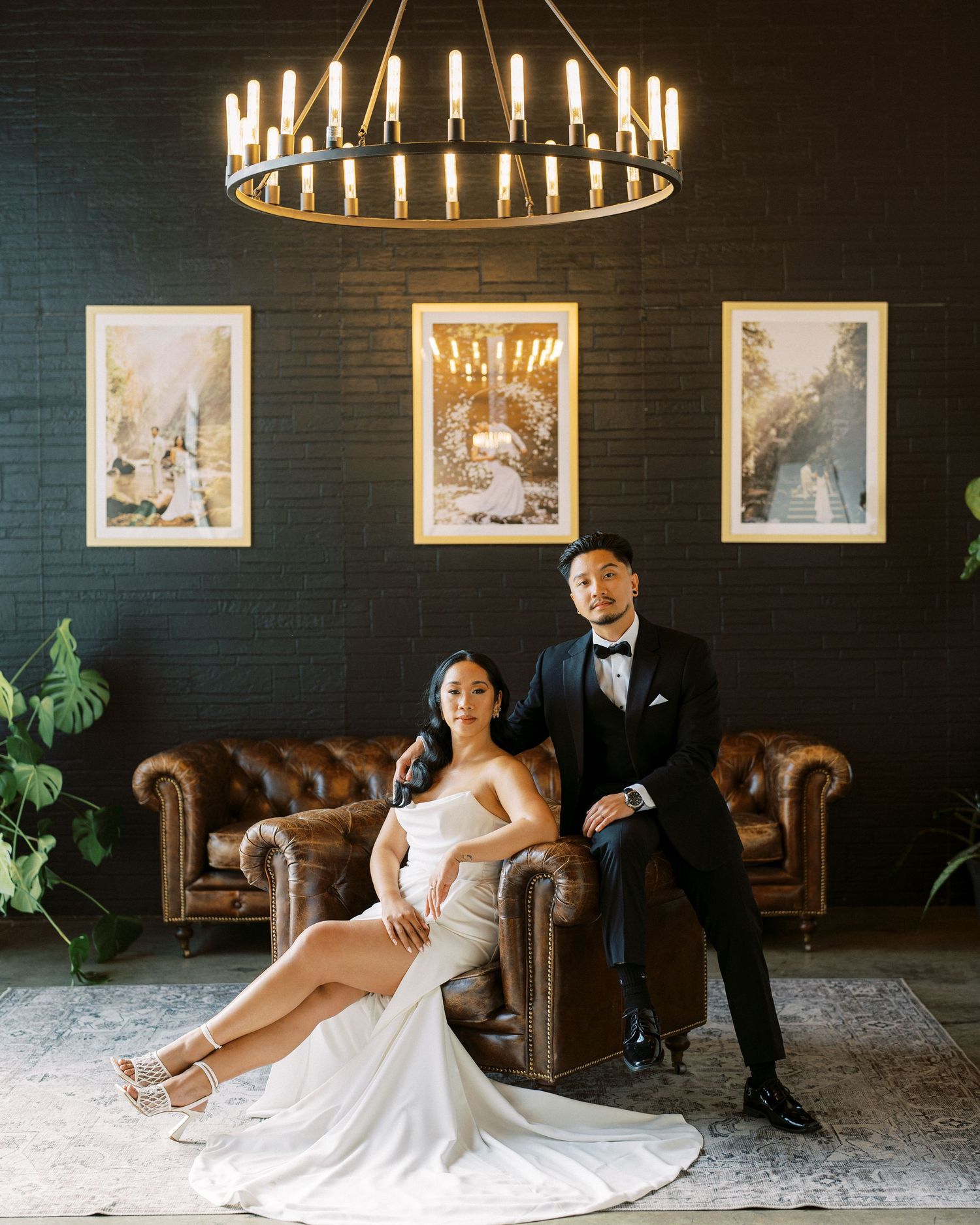 Elegant wedding photo with circular chandelier and leather couch against dark wall.