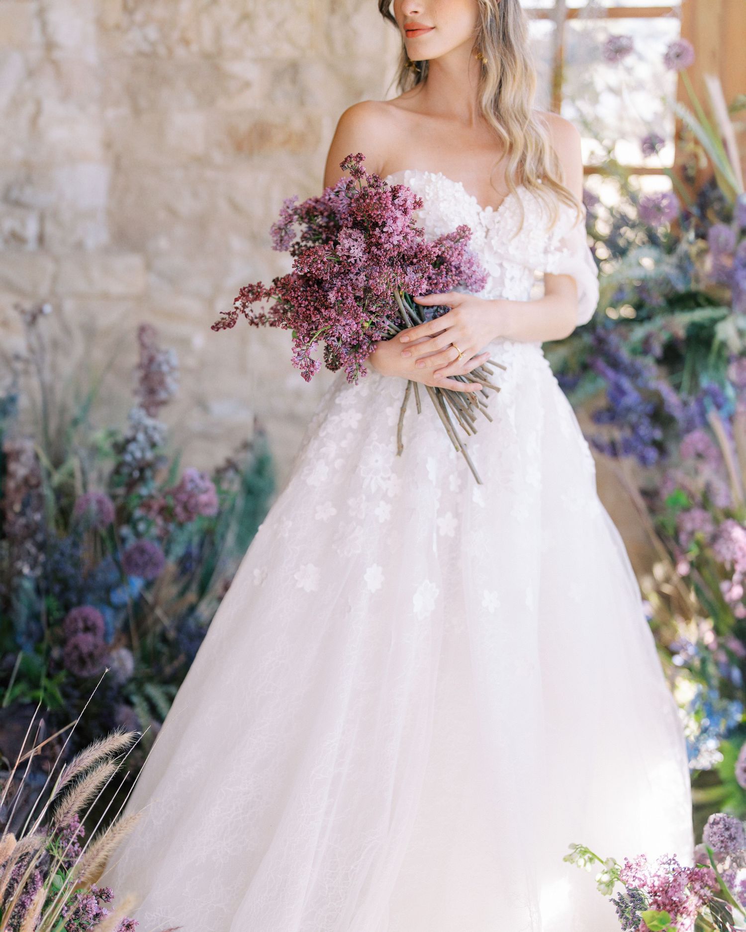 An elegant bridal photo featuring a white gown and purple floral bouquet.