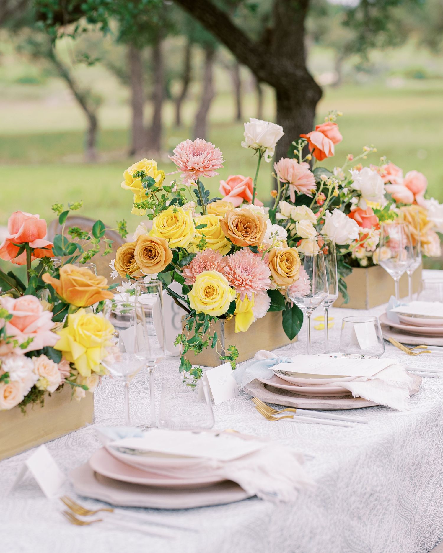 Elegant table setting with pink and yellow roses in floral centerpieces atop white linen tablecloth.