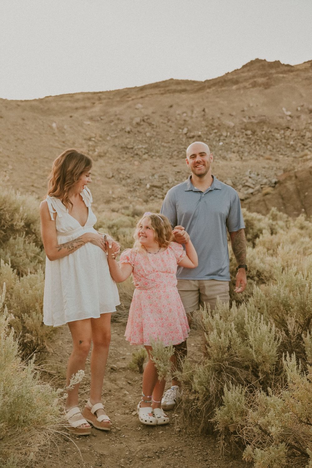 A family enjoying a warm sunset moment together on a desert trail surrounded by sage brush and mountains.
