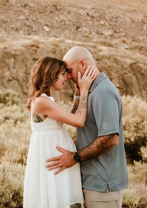 Romantic couple in casual attire share an intimate moment against a desert landscape backdrop.