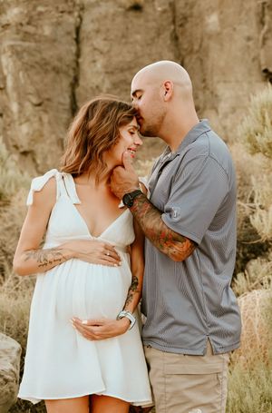 A couple shares an intimate moment outdoors as they celebrate their pregnancy in front of a rocky cliff backdrop.