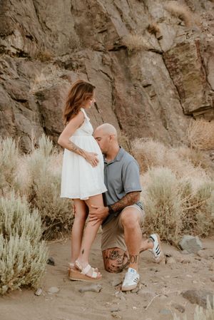 A romantic moment captured in a desert setting with rocky cliffs and sage brush in the background.