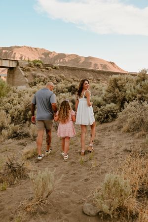 A family walks up a desert trail together with mountains in the background during golden hour.