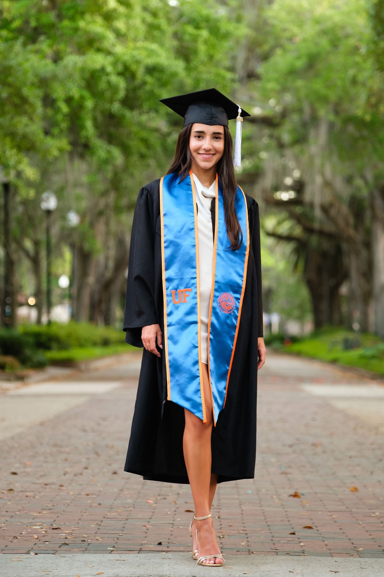 A smiling UF grad in full regalia poses for a portrait at the Plaza of The Americas.
