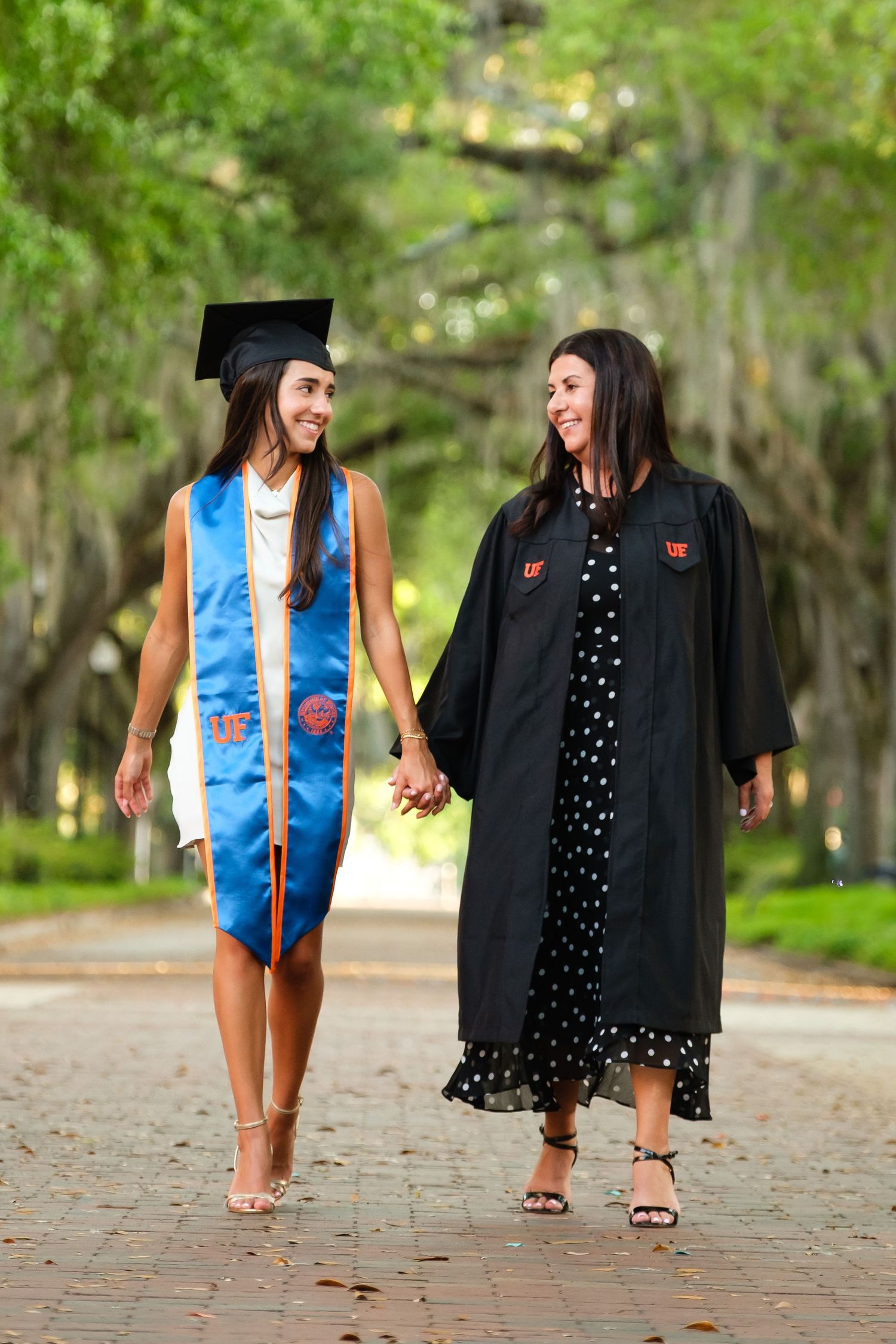 Mother and daughter walk hand in hand smiling at each other during a UF grad session.