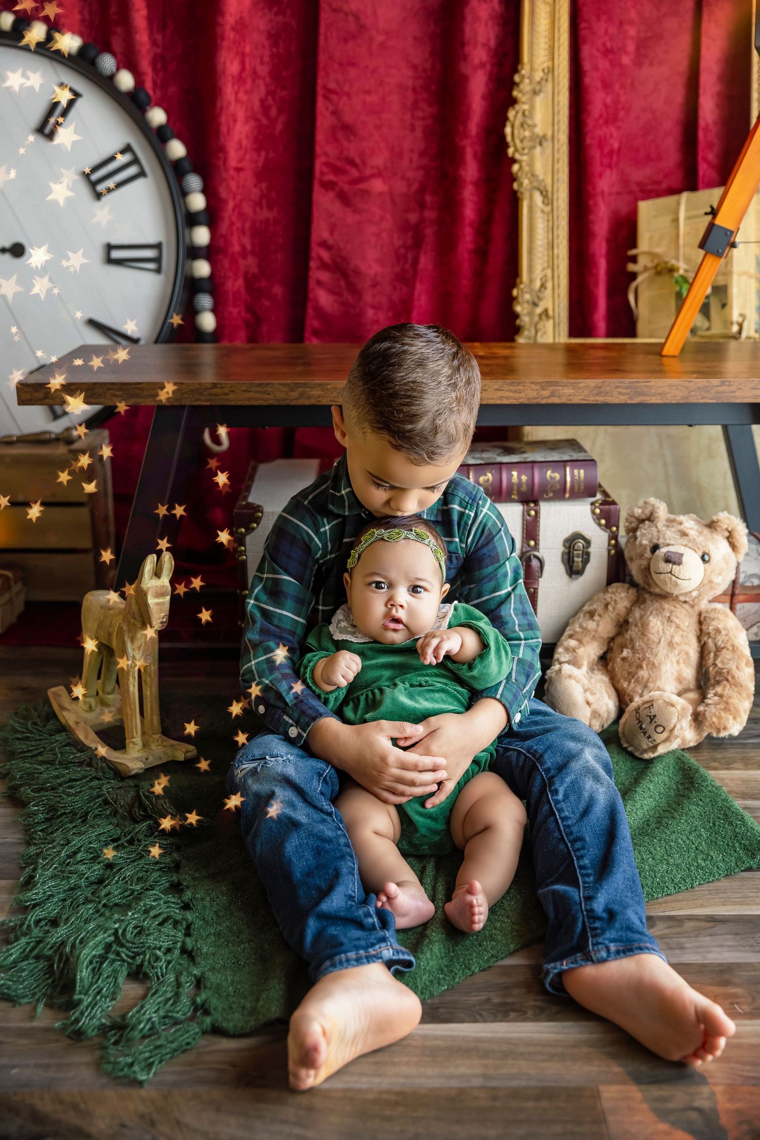 big brother kisses baby sister on the head sitting on the floor portrait