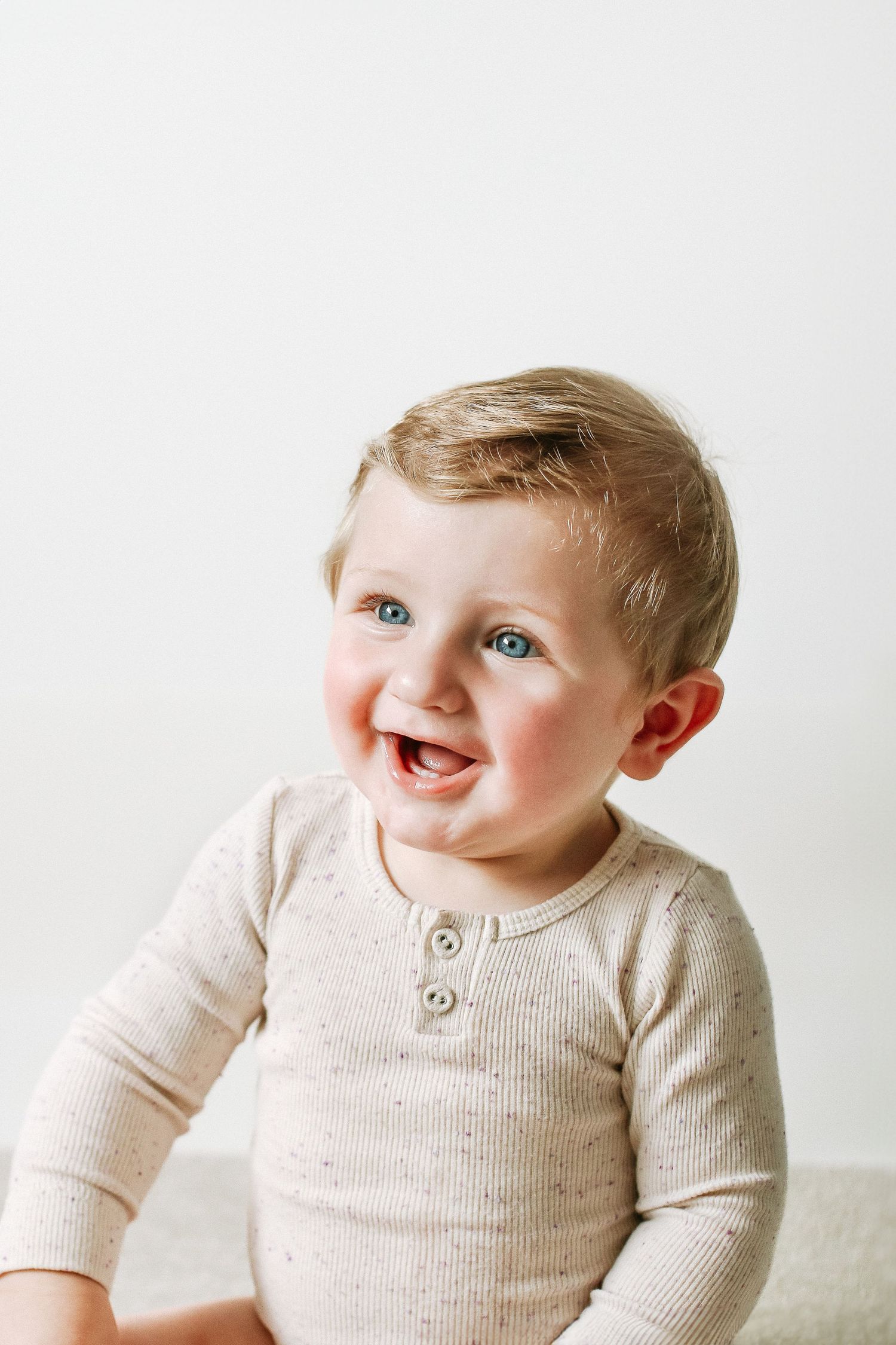 Baby wearing cream coloured sweater showing  playful expressions against white background during birthday shoot in Nottingham