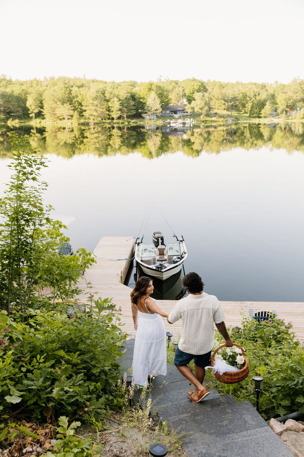 A romantic lakeside scene with two people sitting on rocks overlooking calm waters at sunset.