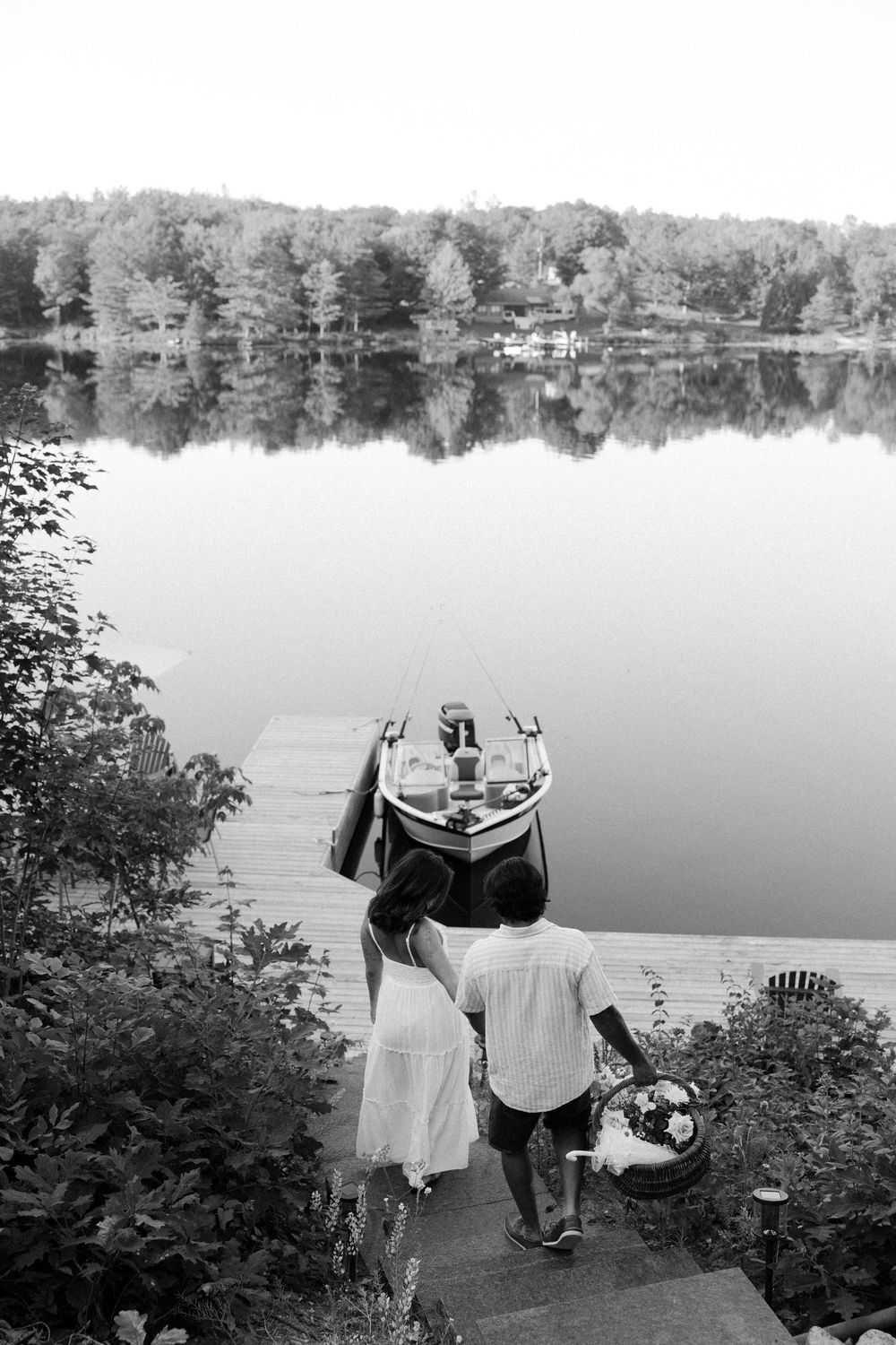 A scenic lake view with people descending stairs carrying supplies toward a boat on a calm summer day.