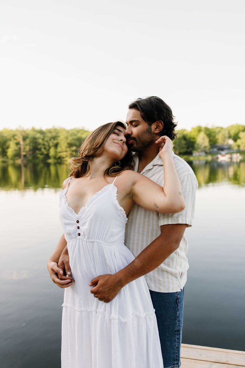 A couple shares an intimate moment on a lakeside dock during a summer photoshoot.