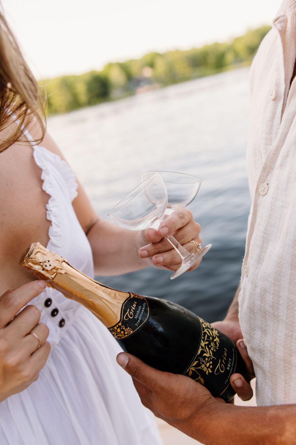 Opening a champagne bottle by the lake during a sunset celebration.