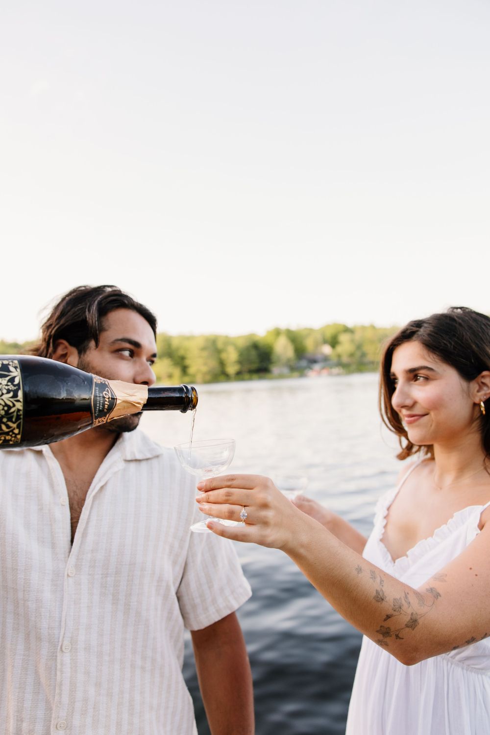 A couple sharing champagne by the lake at golden hour.