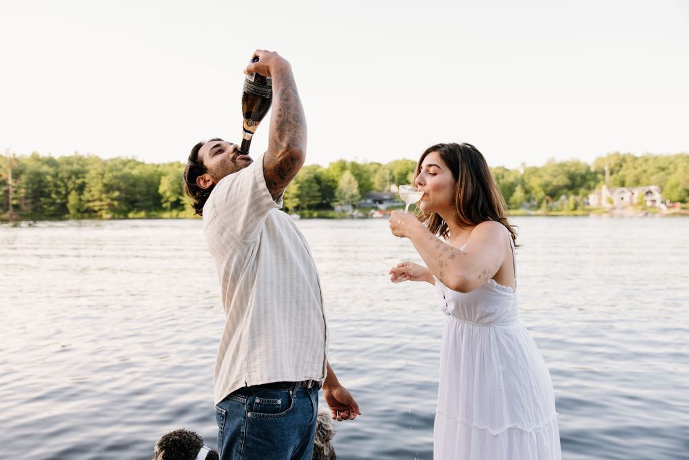 A romantic couple dances and embraces near a tranquil lake during sunset, their joyful movements captured in motion.