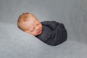 Professional newborn portrait with baby sleeping peacefully on gray backdrop.