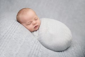 Newborn baby sleeping on textured white blanket in minimalist studio setting.