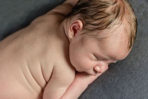 Side profile of sleeping newborn on soft gray backdrop with natural lighting.