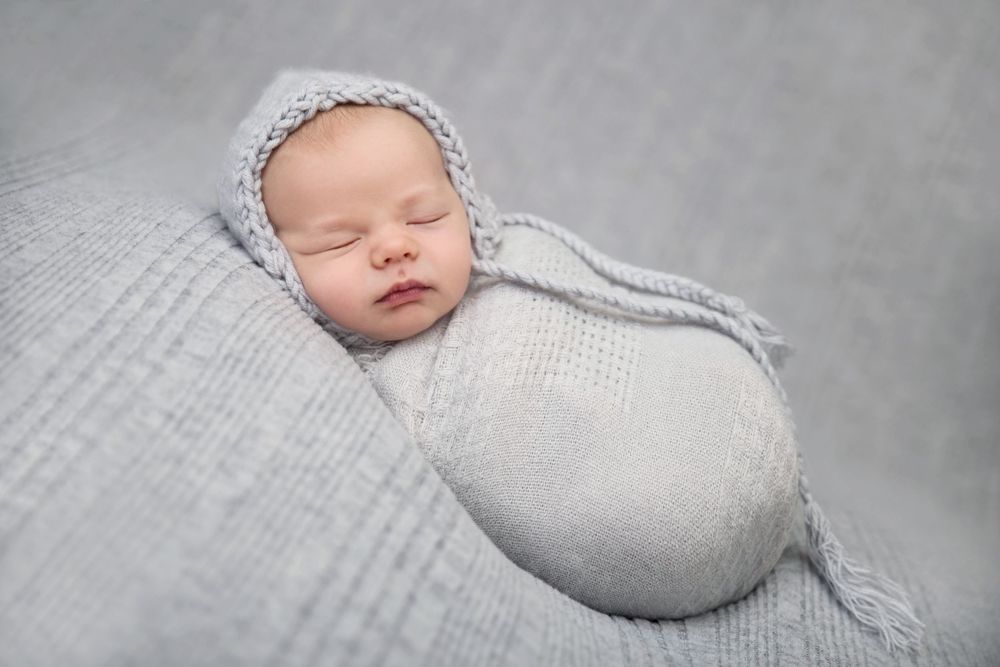 Peaceful newborn wrapped in light gray knit blanket during studio session.