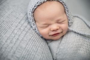 Baby wearing knit gray hat sleeping on textured gray blanket.