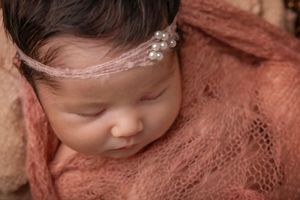 Newborn baby wrapped in pink lace fabric sleeping peacefully during professional photo session.