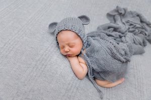 Artistic newborn portrait with gray knit accessories on textured gray background.