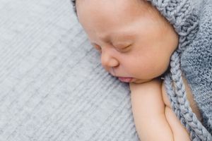 Sleeping baby with gray knit accessories on soft textured backdrop.